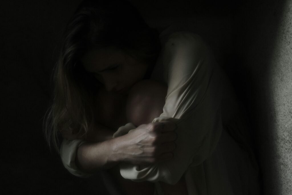 A woman sits in a dimly lit corner, evoking feelings of solitude and introspection.